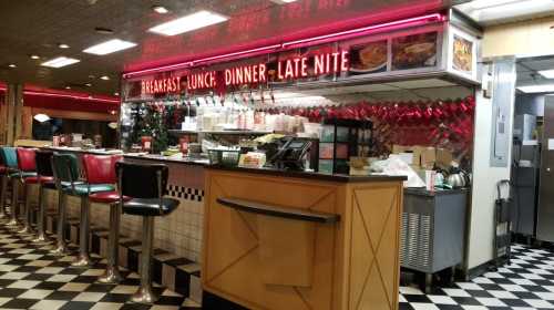 A retro diner interior with a checkered floor, neon signs, and a counter with colorful stools.