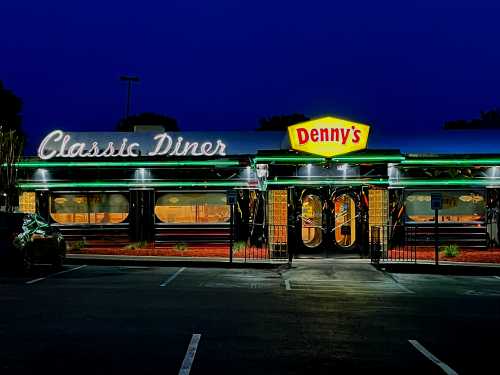 A brightly lit Denny's diner at night, featuring a classic design and neon signage.