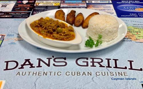 A plate of Cuban cuisine featuring rice, plantains, and a savory meat dish, set on a colorful restaurant table.