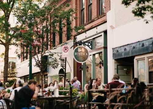 Outdoor dining scene at a restaurant called Rustica, with patrons enjoying meals on a sunny day.