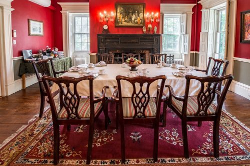 Elegant dining room with a red wall, a large table set for tea, and antique chairs on a patterned rug.