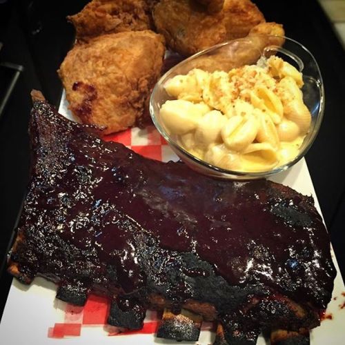 A plate featuring BBQ ribs with sauce, fried chicken pieces, and a side of creamy macaroni and cheese.