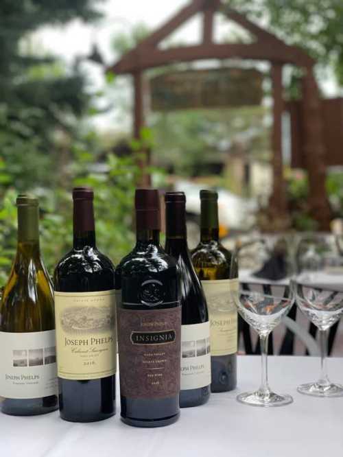 A selection of Joseph Phelps wines on a table, with wine glasses and a blurred outdoor setting in the background.