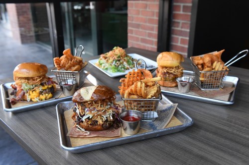 A variety of gourmet burgers and crispy fries served on a wooden table, showcasing different toppings and styles.