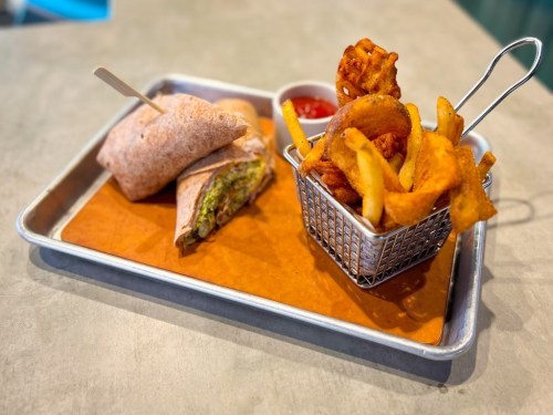 A tray with a wrap, fries in a small basket, and a dipping sauce on the side.
