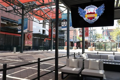 An outdoor dining area with seating and a large screen displaying Guy Fieri's logo in a vibrant urban setting.