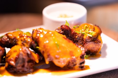 A plate of glazed chicken wings garnished with green onions, served with a small bowl of dipping sauce.
