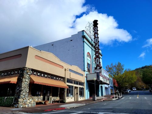 A quaint street scene featuring a bakery and a vintage theater with a "California" marquee under a blue sky.