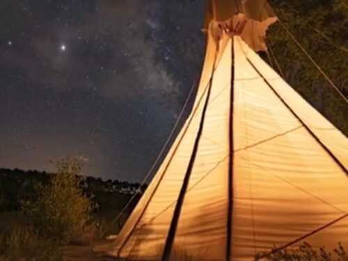 A lit teepee under a starry night sky, with the Milky Way visible in the background.