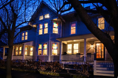 A cozy house at dusk, featuring colorful stained glass windows and a welcoming porch surrounded by bare trees.