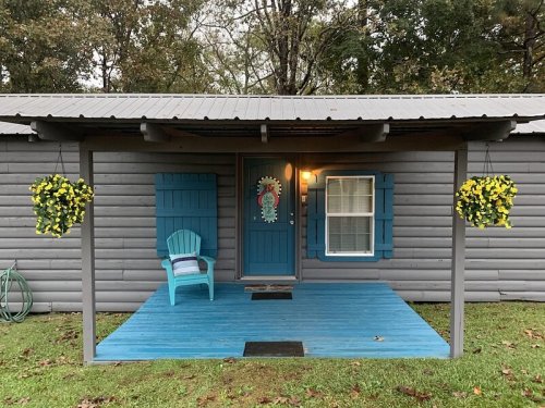 A cozy cabin with a blue porch, yellow flower baskets, and a welcoming front door surrounded by trees.