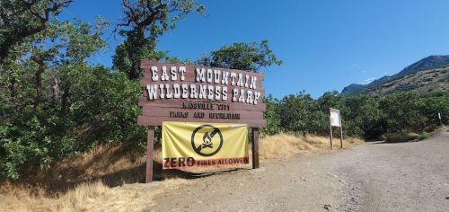 Sign for East Mountain Wilderness Park with a warning banner stating "ZERO Fires Allowed" and surrounding greenery.