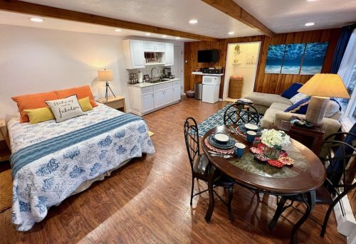 Cozy studio apartment with a bed, kitchenette, dining table, and seating area, featuring warm lighting and beach decor.