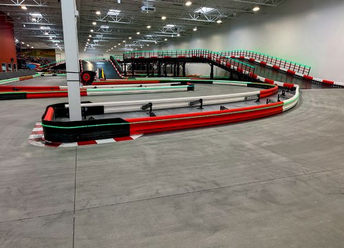 Indoor go-kart track with winding lanes, red and green barriers, and a smooth concrete surface.