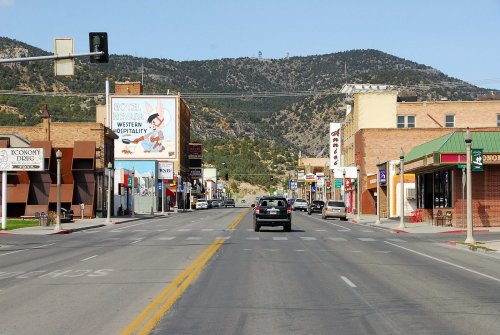 A quiet street scene with shops and signs, flanked by mountains in the background under a clear blue sky.