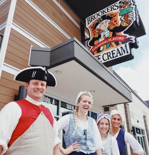 Four people in historical costumes stand outside Brooker's Ice Cream, smiling in front of a colorful sign.