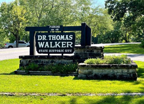 Sign for Dr. Thomas Walker State Historic Site, featuring a parking area and green landscaping.