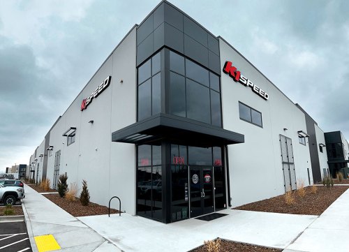Exterior view of a modern building with "K1 Speed" signage, featuring large windows and an "OPEN" sign at the entrance.