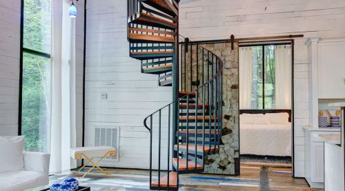 A modern interior featuring a spiral staircase, white walls, and a cozy bedroom visible through an open doorway.