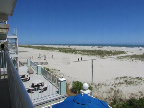 A beach view with sandy dunes, a clear blue sky, and people walking along the shore in the distance.