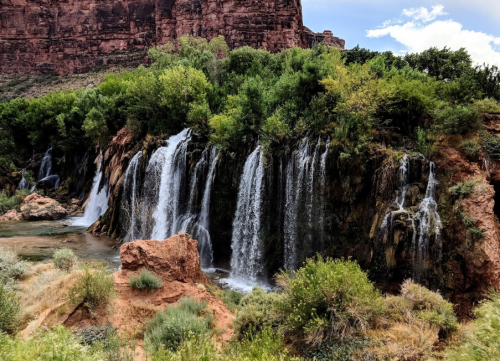 A scenic view of cascading waterfalls surrounded by lush greenery and rocky cliffs under a blue sky.