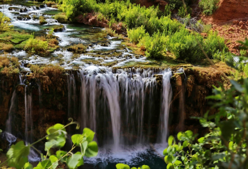 A serene waterfall cascading over rocks, surrounded by lush greenery and a tranquil blue pool below.