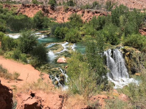 A serene landscape featuring a turquoise river with waterfalls, surrounded by lush greenery and rocky terrain.