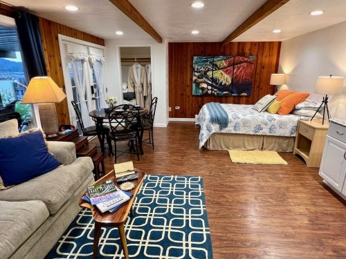 Cozy studio apartment with a bed, dining area, and living space featuring warm wood accents and colorful decor.