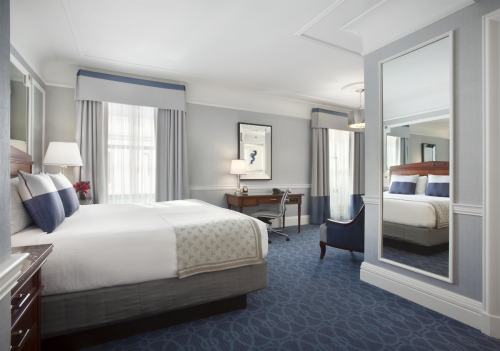 A modern hotel room featuring a king bed, desk, chair, and large mirror, with soft lighting and elegant decor.