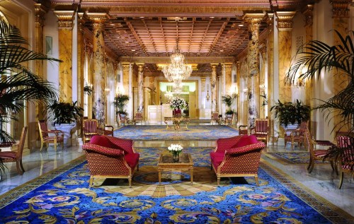 Luxurious hotel lobby with ornate decor, plush red chairs, a chandelier, and vibrant floral carpets.