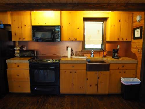 A cozy kitchen with wooden cabinets, a black stove, sink, and appliances, illuminated by warm lighting.
