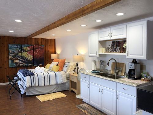 Cozy studio apartment with a bed, kitchenette, and wooden accents, featuring warm lighting and colorful decor.
