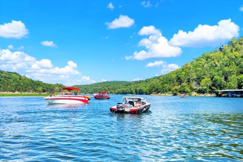 Boats on a sunny lake surrounded by green hills and a blue sky with fluffy clouds.