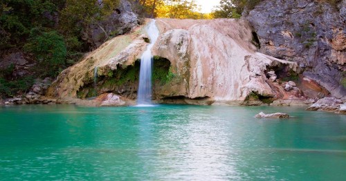 A serene waterfall cascading over rocky terrain into a turquoise pool, surrounded by lush greenery.