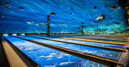 A vibrant bowling alley with an underwater-themed ceiling and lanes featuring oceanic designs and colorful marine life.
