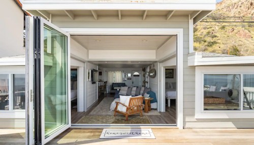 Cozy beach house interior with open doors, inviting natural light and ocean views. Stylish decor and comfortable seating.