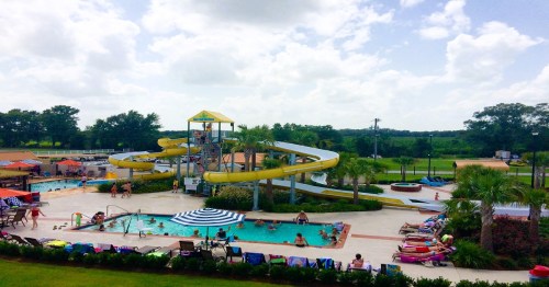 A vibrant water park scene featuring a large yellow waterslide, pools, and people enjoying the sun.