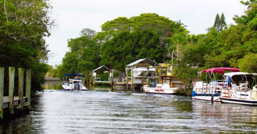 A serene waterway lined with lush greenery and boats docked along wooden piers.