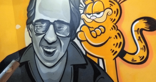 A mural featuring a smiling man in grayscale next to a mischievous orange cat, set against a bright orange background.