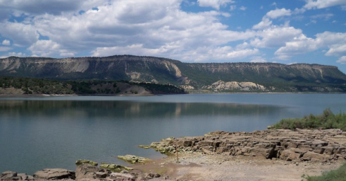 A serene lake surrounded by rocky shores and mountains under a partly cloudy sky.