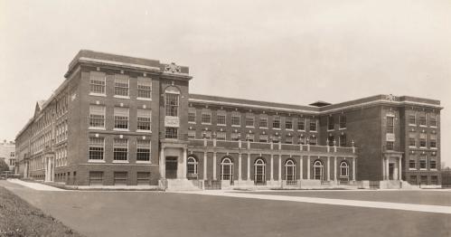 Historic brick building with large windows and a symmetrical facade, set against a clear sky.