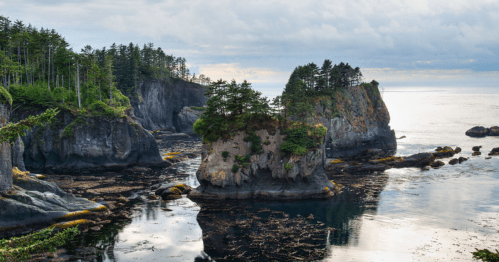 A serene coastal landscape featuring rocky islands, lush greenery, and calm waters under a cloudy sky.