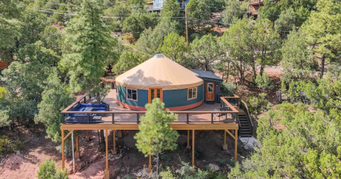 A cozy yurt on a raised deck surrounded by trees, featuring outdoor seating and a scenic view.