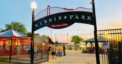 Entrance to Kiddie Park in Bartlesville, featuring a colorful carousel and people enjoying the evening atmosphere.