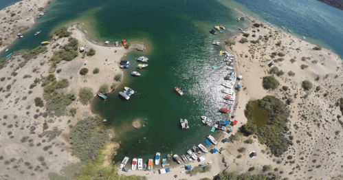 Aerial view of a serene bay with boats anchored along a sandy shore and lush greenery surrounding the water.