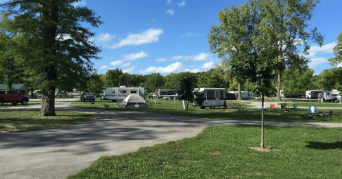 A campsite with RVs and tents surrounded by trees under a blue sky with scattered clouds.