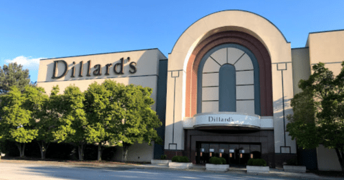 Exterior of a Dillard's department store with a large entrance and trees in front, under a clear blue sky.