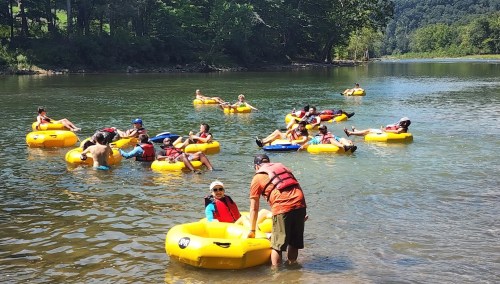 A group of people floating on yellow inner tubes in a river, enjoying a sunny day surrounded by trees.