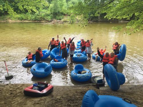 A group of people in life jackets enjoying a river tubing adventure, surrounded by blue inflatable tubes and greenery.