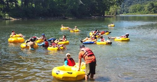 People floating on yellow inner tubes in a river, enjoying a sunny day surrounded by trees and water.